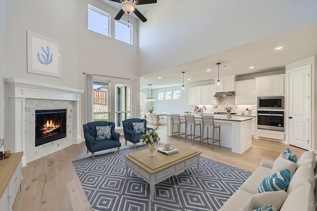 living room featuring ceiling fan, a high end fireplace, and light hardwood / wood-style flooring