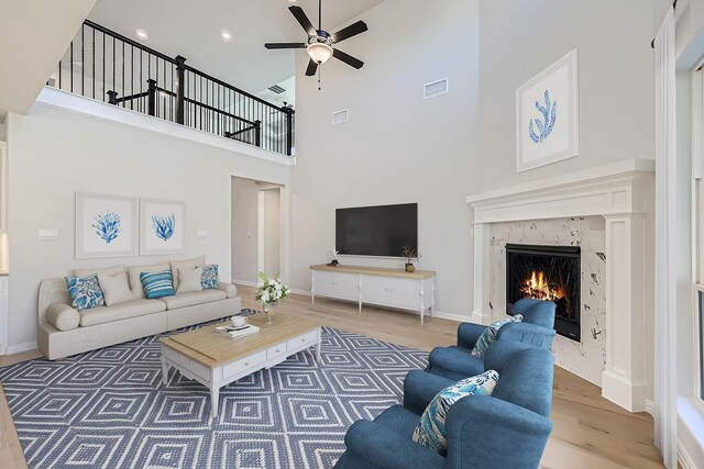 living room featuring a high end fireplace, wood-type flooring, and ceiling fan