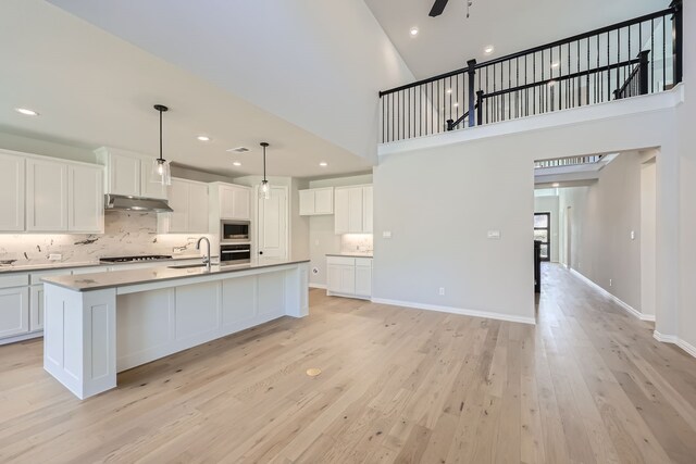 kitchen featuring white cabinetry, appliances with stainless steel finishes, hanging light fixtures, and a center island with sink