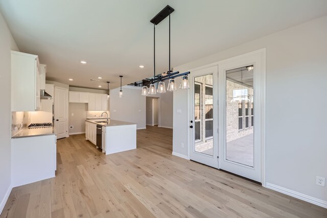 kitchen featuring an island with sink, dishwasher, white cabinets, hanging light fixtures, and stainless steel gas cooktop