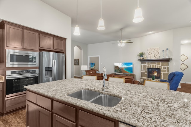 kitchen featuring sink, light stone counters, decorative light fixtures, a fireplace, and appliances with stainless steel finishes