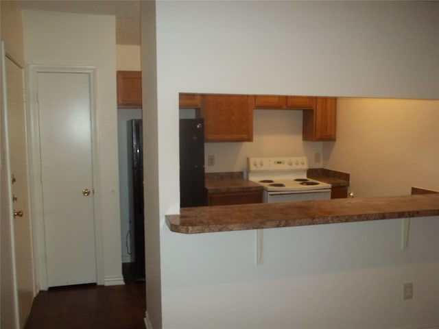 kitchen with white electric range oven, dark hardwood / wood-style flooring, a breakfast bar, and kitchen peninsula