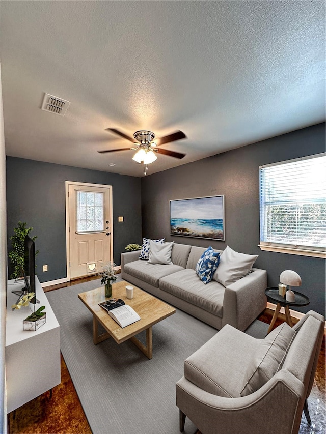 living area featuring ceiling fan, a wealth of natural light, a textured ceiling, and visible vents