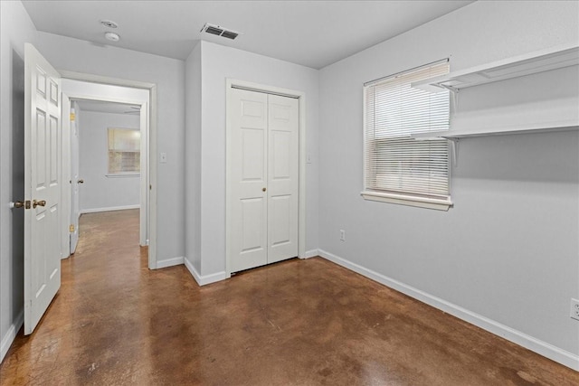 unfurnished bedroom with concrete flooring, a closet, visible vents, and baseboards