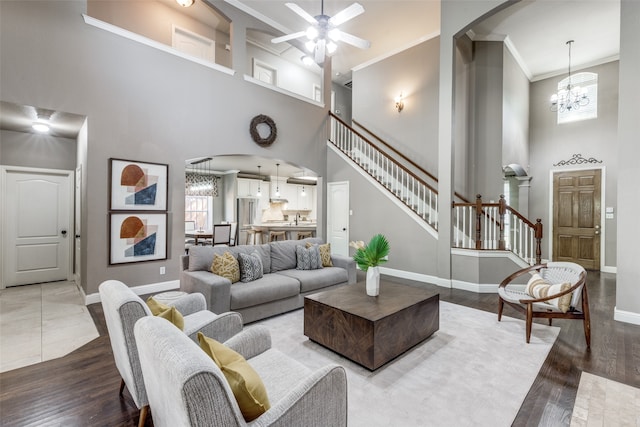 living room featuring a towering ceiling, sink, wood-type flooring, ceiling fan with notable chandelier, and ornamental molding