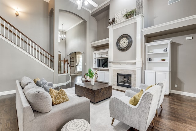 living room featuring hardwood / wood-style flooring, a tile fireplace, built in shelves, a towering ceiling, and crown molding