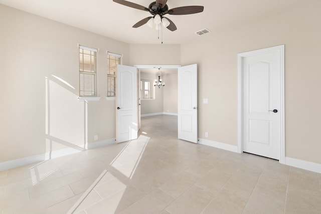 tiled empty room featuring ceiling fan with notable chandelier