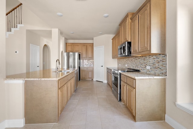 kitchen featuring backsplash, a center island with sink, sink, light stone countertops, and appliances with stainless steel finishes