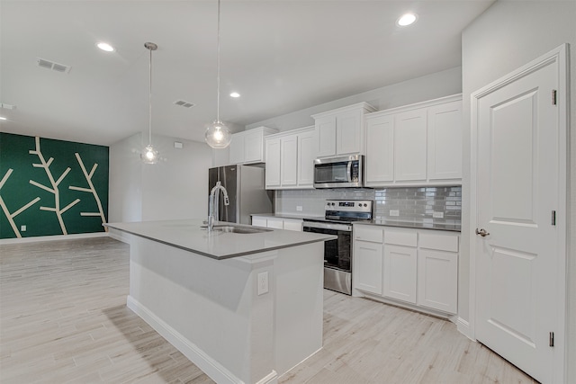 kitchen featuring a kitchen island with sink, white cabinets, hanging light fixtures, and stainless steel appliances