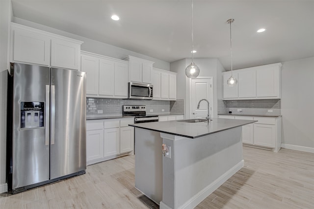 kitchen featuring appliances with stainless steel finishes, sink, white cabinetry, decorative light fixtures, and a kitchen island with sink