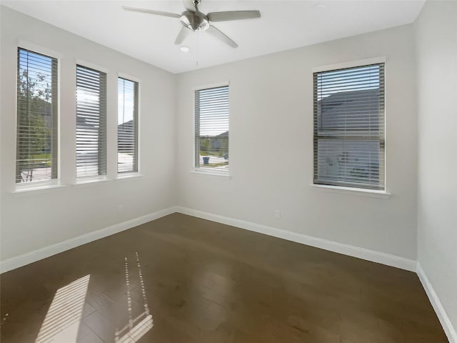 empty room featuring dark wood-type flooring, a ceiling fan, baseboards, and a healthy amount of sunlight