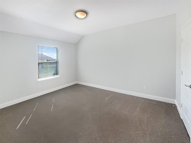 spare room featuring vaulted ceiling, dark colored carpet, and baseboards