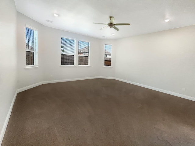 empty room with a ceiling fan, visible vents, dark colored carpet, and baseboards