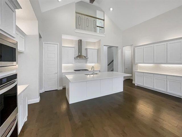 kitchen with wall chimney exhaust hood, a kitchen island with sink, high vaulted ceiling, and dark hardwood / wood-style flooring