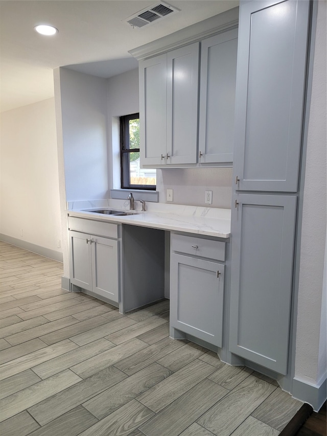 kitchen with gray cabinets, light stone countertops, sink, and light wood-type flooring