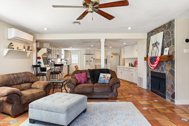 living room with a stone fireplace, a wall unit AC, tile patterned flooring, and ceiling fan