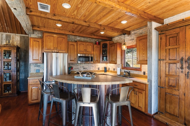 kitchen with beam ceiling, a kitchen island with sink, stainless steel appliances, and dark hardwood / wood-style floors