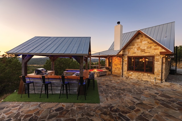 patio terrace at dusk with a gazebo, a jacuzzi, and grilling area