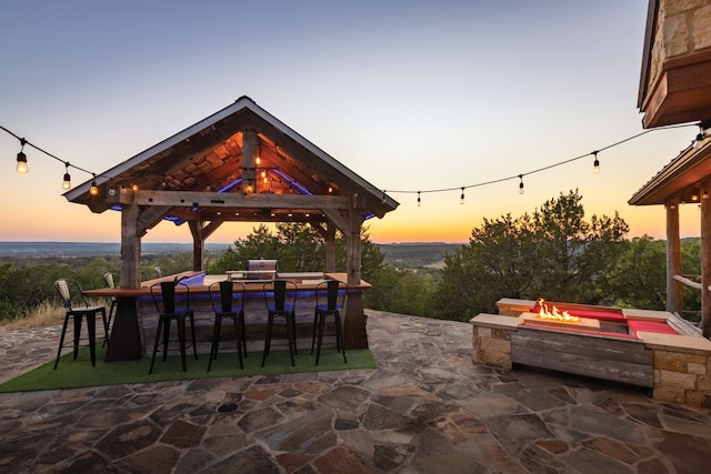 patio terrace at dusk with an outdoor fire pit, a gazebo, and exterior bar