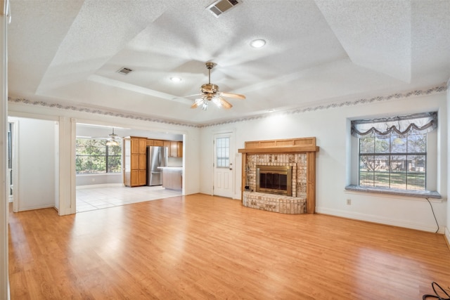 unfurnished living room featuring a tray ceiling, a fireplace, light hardwood / wood-style floors, and ceiling fan