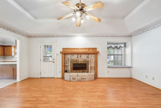 unfurnished living room featuring a raised ceiling, a brick fireplace, and light hardwood / wood-style floors