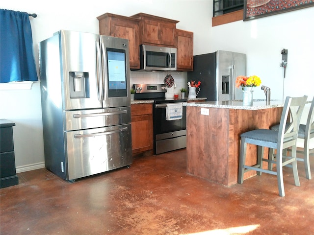 kitchen with light stone countertops, appliances with stainless steel finishes, a breakfast bar area, and decorative backsplash