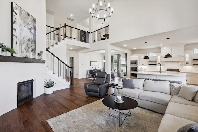 living room featuring dark wood-type flooring, sink, a notable chandelier, a high ceiling, and a tiled fireplace