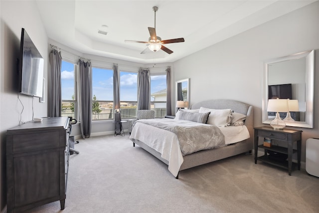 carpeted bedroom with a raised ceiling and ceiling fan