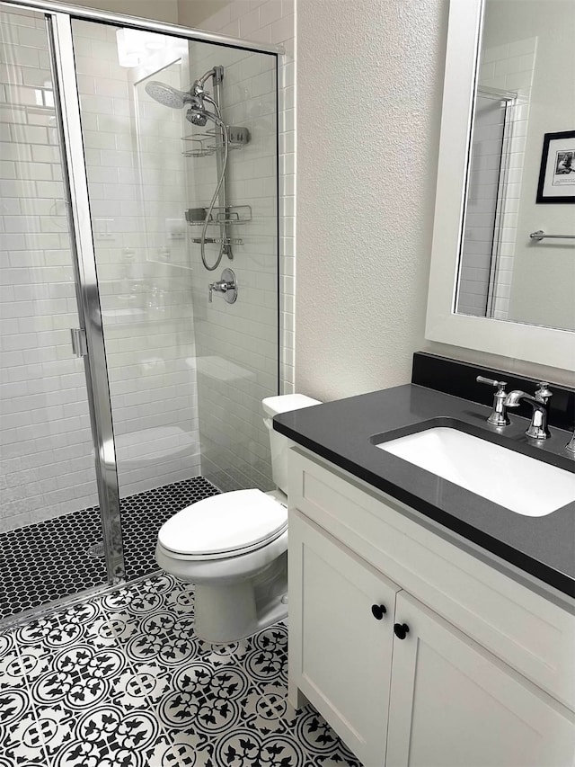 bathroom featuring tile patterned flooring, vanity, toilet, and a shower with shower door