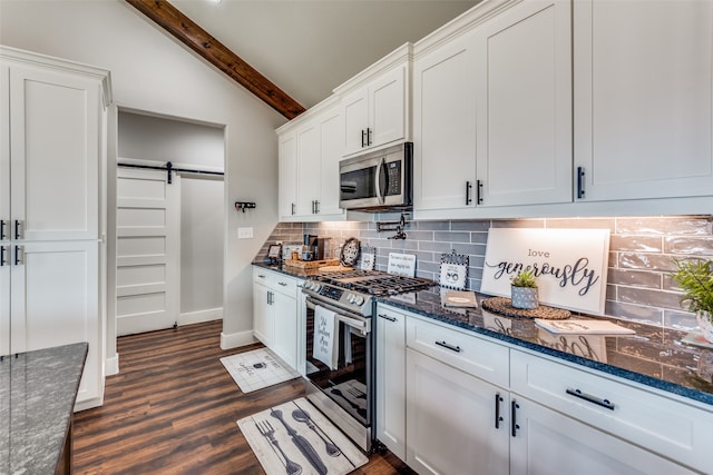 kitchen featuring decorative backsplash, white cabinets, a barn door, lofted ceiling with beams, and stainless steel appliances