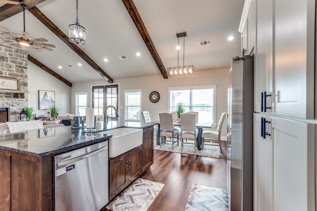 kitchen with appliances with stainless steel finishes, a kitchen island with sink, dark stone countertops, dark wood-type flooring, and sink