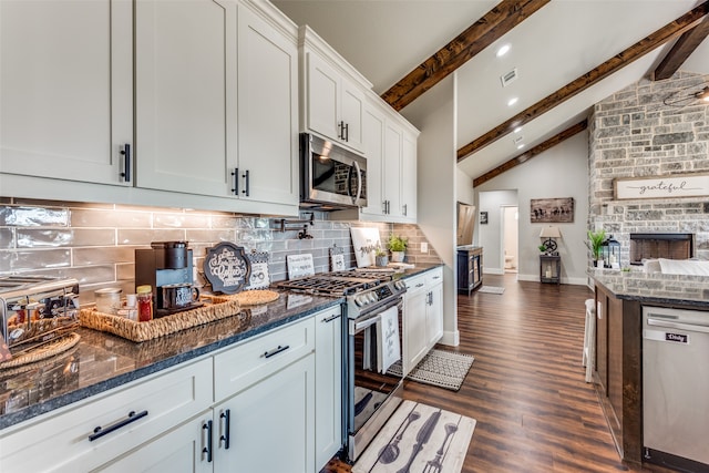 kitchen featuring tasteful backsplash, vaulted ceiling with beams, stainless steel appliances, white cabinets, and dark stone countertops