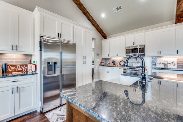 kitchen with white cabinets, vaulted ceiling with beams, stainless steel appliances, and dark stone counters