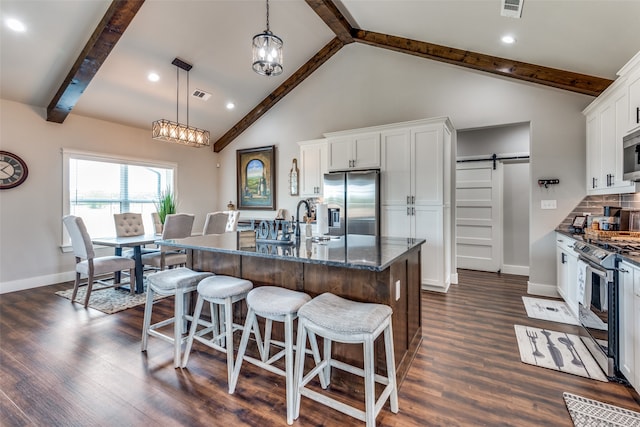 kitchen featuring appliances with stainless steel finishes, white cabinetry, a barn door, and a center island with sink