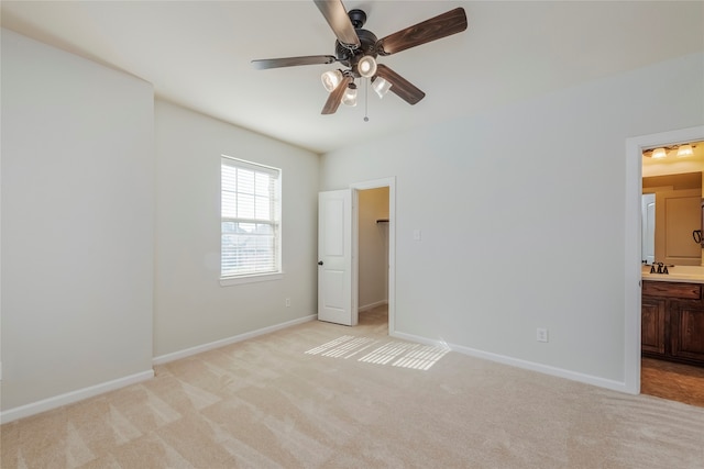 unfurnished bedroom featuring a walk in closet, ensuite bath, light colored carpet, and ceiling fan