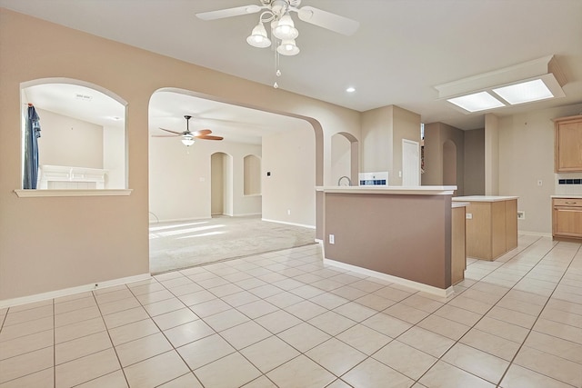 kitchen with light brown cabinets, a center island, light carpet, and ceiling fan