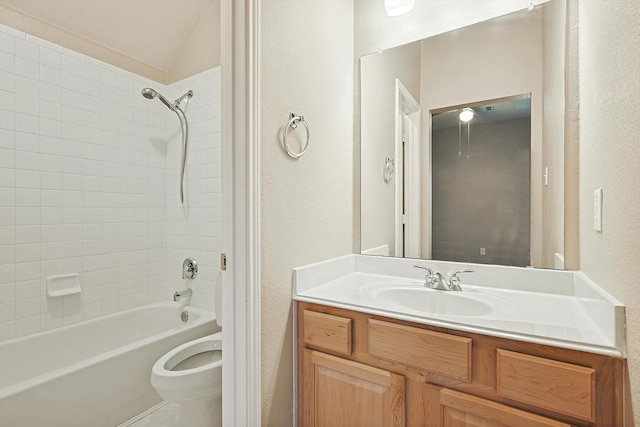 full bathroom with tiled shower / bath, vanity, vaulted ceiling, and toilet