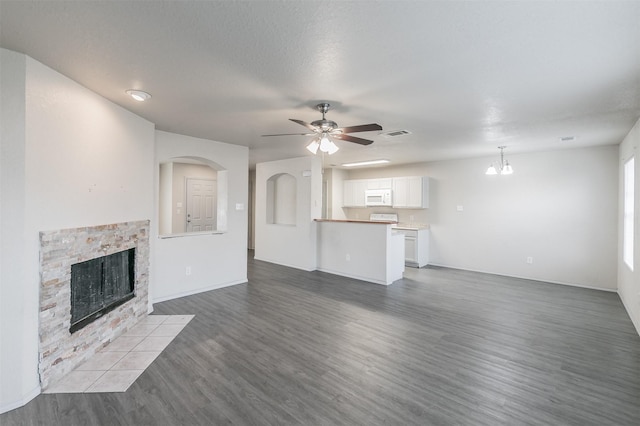 unfurnished living room featuring a textured ceiling, a stone fireplace, hardwood / wood-style floors, and ceiling fan with notable chandelier