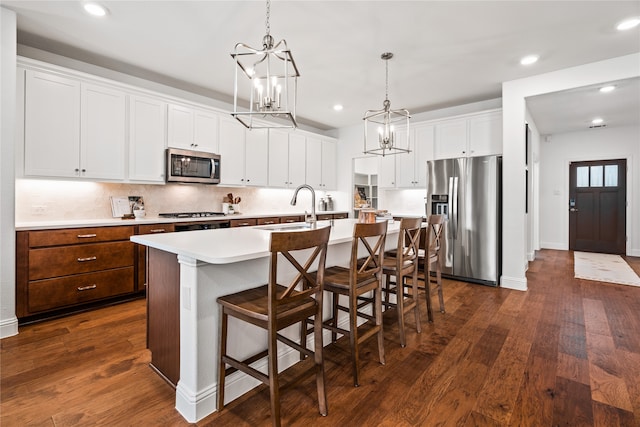 kitchen featuring a breakfast bar, sink, white cabinets, stainless steel appliances, and a center island with sink