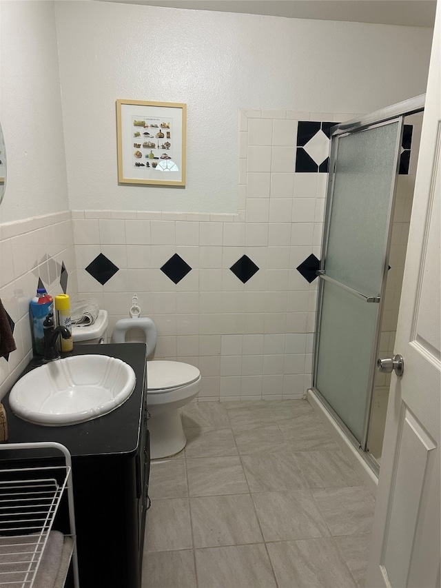 bathroom featuring tile patterned floors, toilet, vanity, tile walls, and an enclosed shower