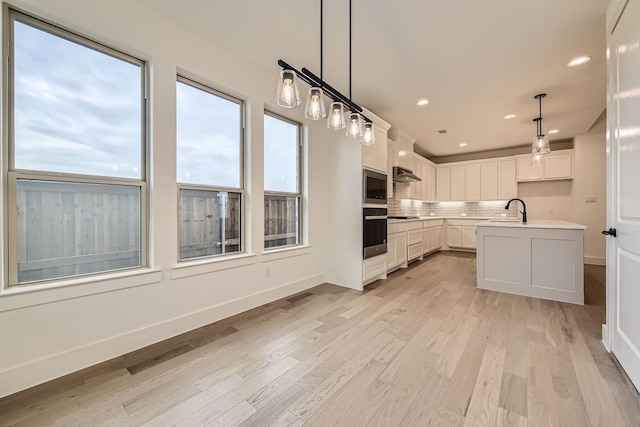 kitchen featuring decorative light fixtures, white cabinetry, decorative backsplash, a kitchen island with sink, and black appliances