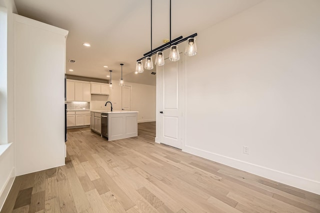 kitchen featuring white cabinetry, hanging light fixtures, a kitchen island with sink, stainless steel dishwasher, and light hardwood / wood-style floors