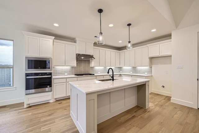 kitchen with pendant lighting, sink, white cabinetry, stainless steel appliances, and a center island with sink