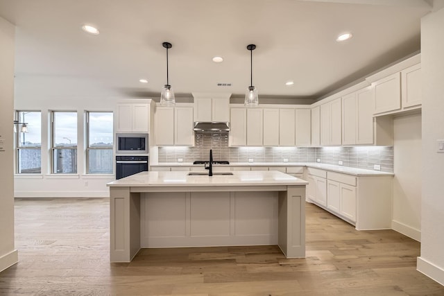 kitchen featuring stainless steel microwave, oven, an island with sink, and white cabinets