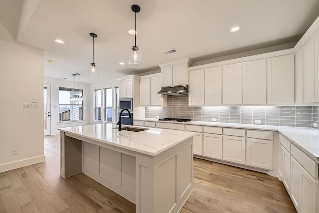 kitchen featuring light stone counters, sink, pendant lighting, and an island with sink