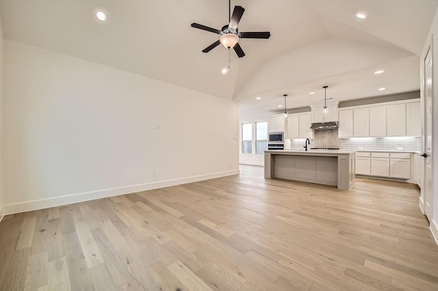 kitchen with lofted ceiling, white cabinetry, hanging light fixtures, an island with sink, and backsplash