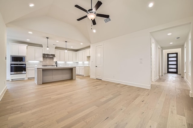 kitchen featuring pendant lighting, stainless steel appliances, an island with sink, white cabinets, and decorative backsplash