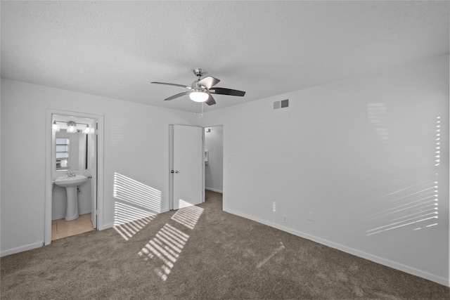 unfurnished bedroom with carpet flooring, a textured ceiling, sink, connected bathroom, and ceiling fan