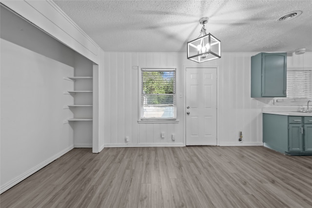 unfurnished dining area featuring a textured ceiling, built in features, sink, and light hardwood / wood-style flooring