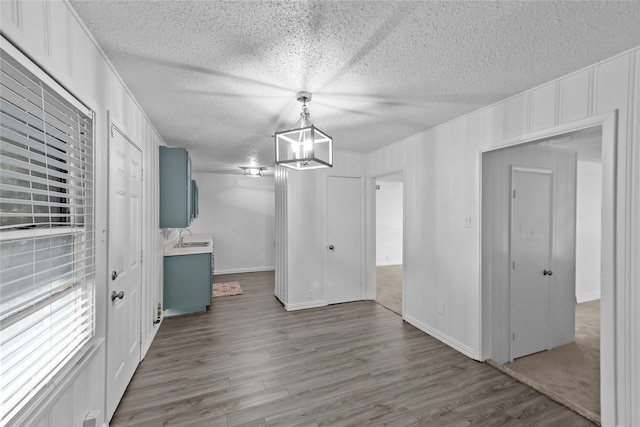 unfurnished dining area with wood-type flooring, a textured ceiling, sink, and a chandelier